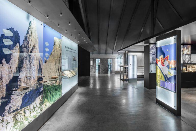 Foto von einem Ausstellungs·saal im Museum Ciastel de Tor. An den Wänden sind Bilder zu sehen. Im Raum stehen Info-Points.