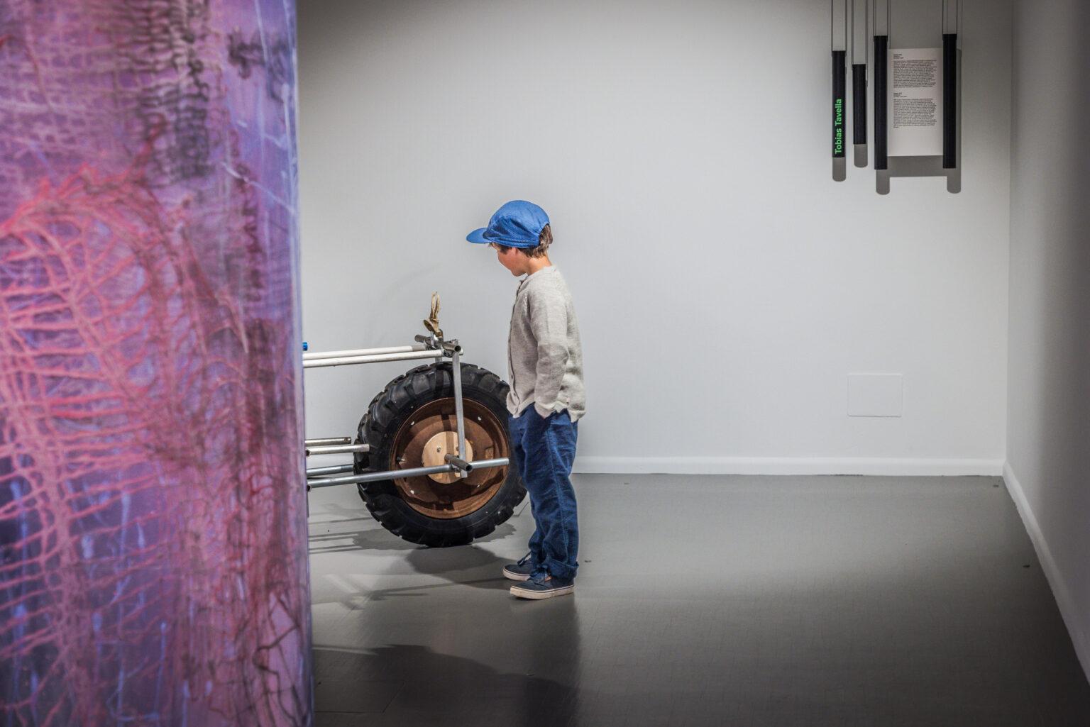 Un bambino osserva un’installazione artistica in uno spazio museale o espositivo.